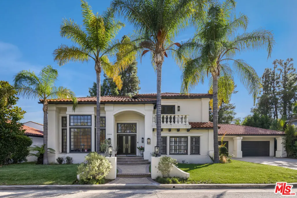 Luxury two-story Mediterranean-style villa featuring a white stucco exterior, tall palm trees, elegant arched entrance, black-framed windows, and landscaped front yard.